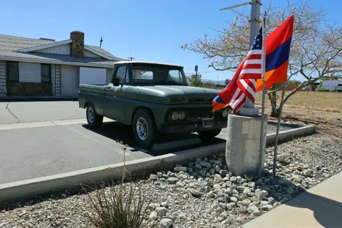 Vintage green pickup truck parked beside American and Armenian flags at the church car show