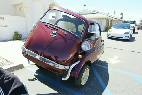 Burgundy BMW Isetta microcar parked in front of the church