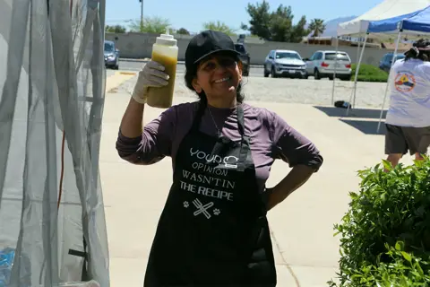 Volunteer in an apron raising a cup of tan drink with a smile