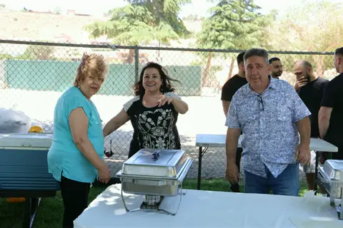 Three smiling parishioners serving food from chafing dishes at the buffet line