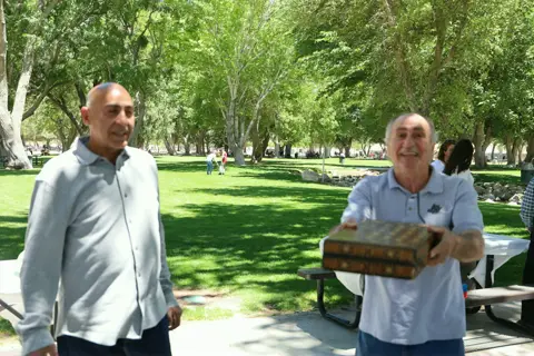 Two men carrying a backgammon board across the park lawn