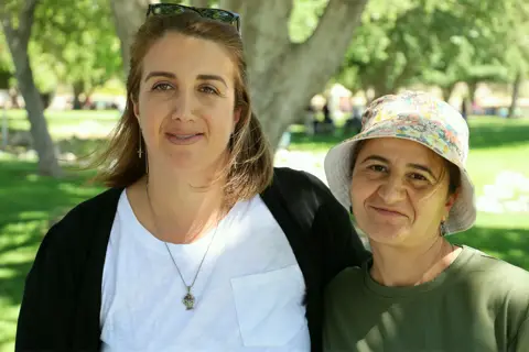 Two women of the parish smiling together under the park trees